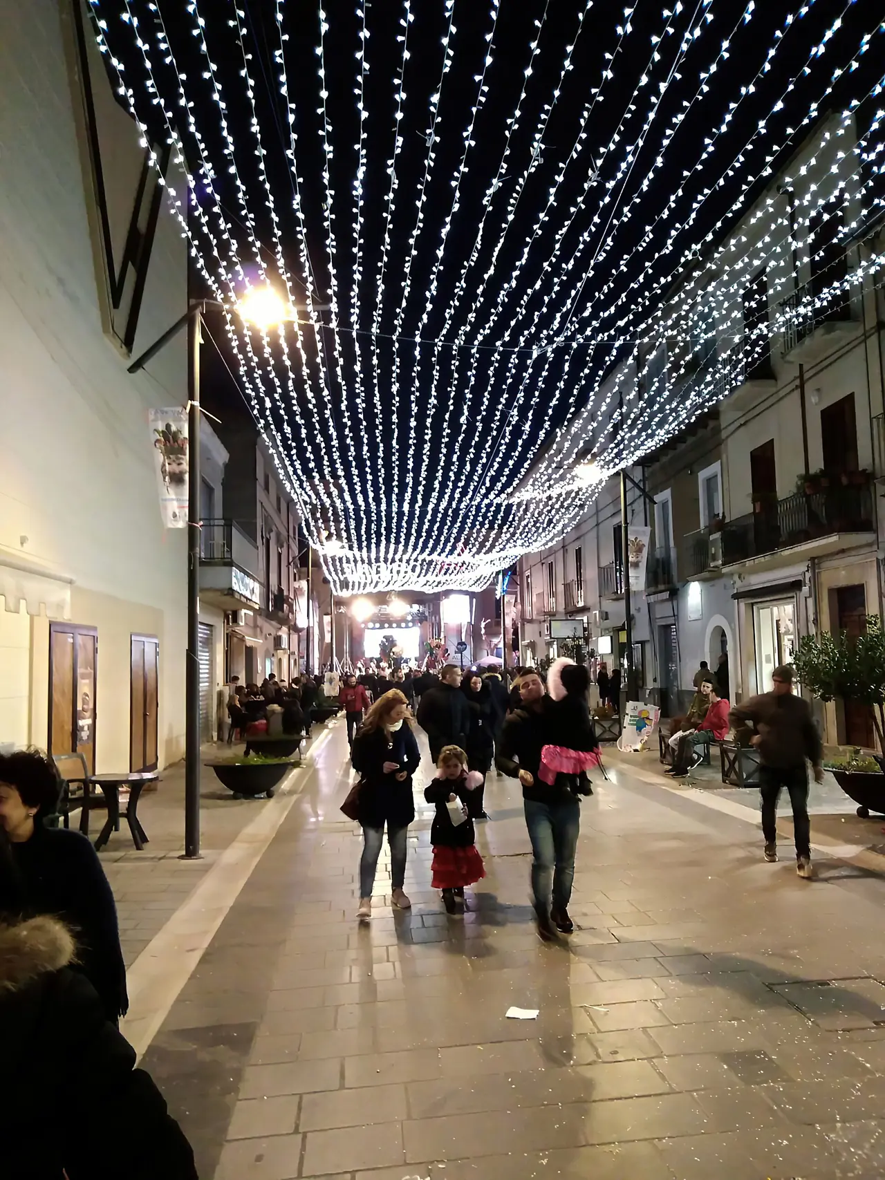 Via del centro coperta da una volta di luci bianche con passanti
