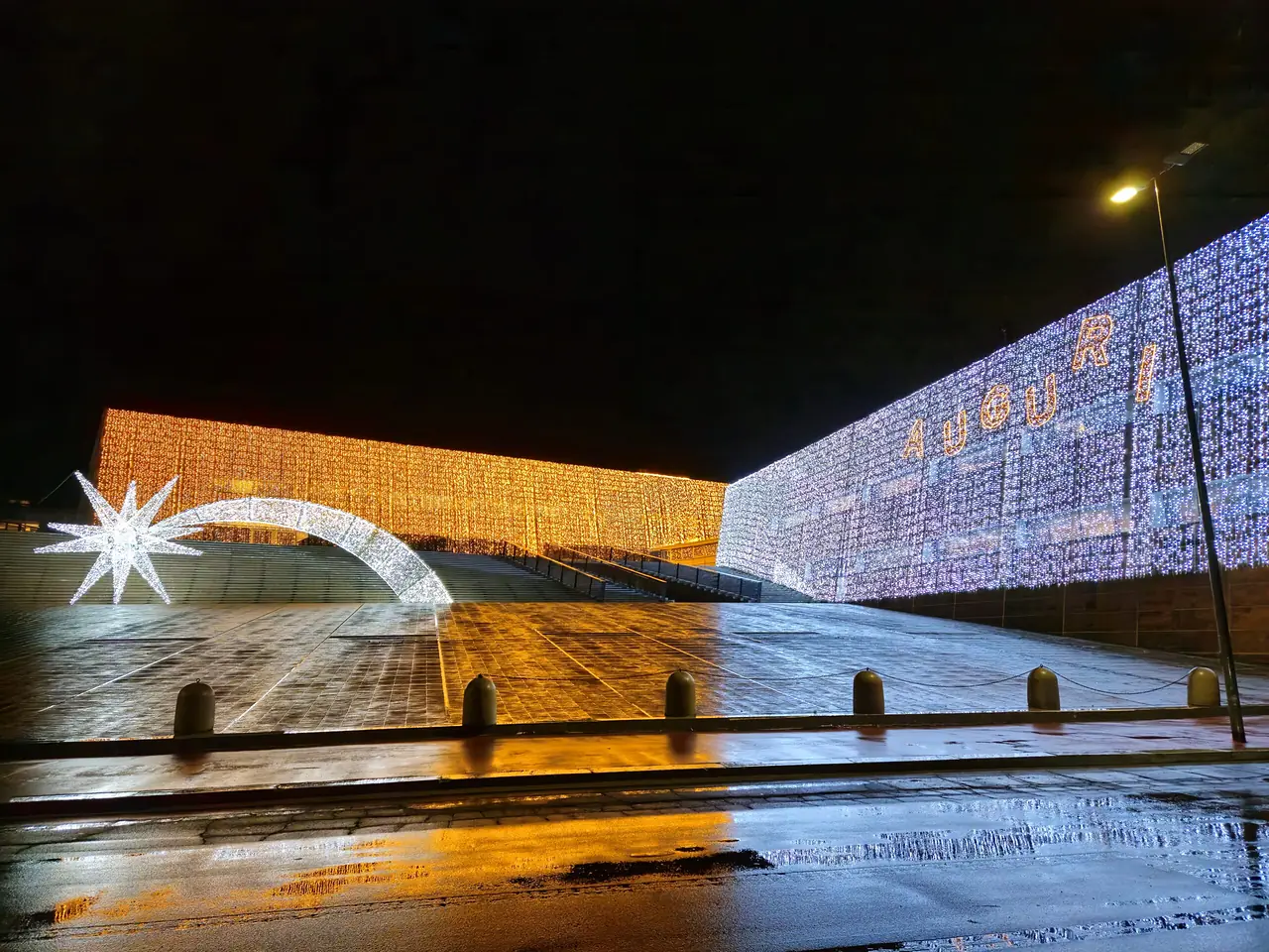 Lungo muro di luci dorate con una cometa luminosa riflessa sul selciato bagnato