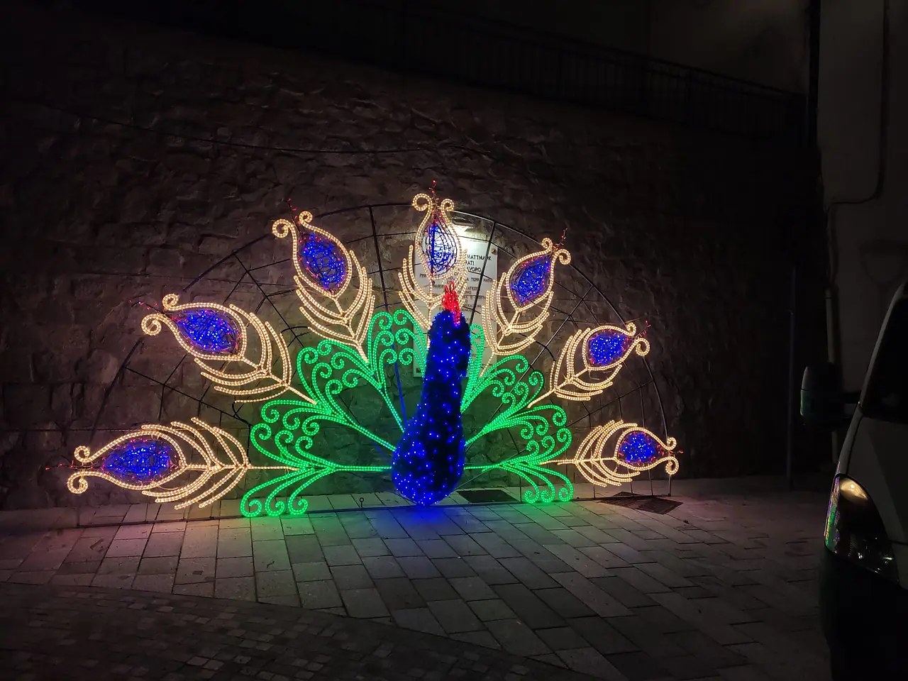Pavone luminoso con la coda aperta in luci verdi, blu e oro